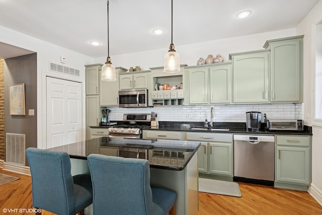 kitchen featuring appliances with stainless steel finishes, a sink, tasteful backsplash, a kitchen bar, and light wood-style floors