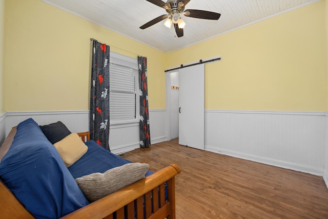 living area with a wainscoted wall, a barn door, wood finished floors, ceiling fan, and ornamental molding