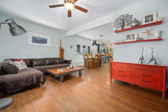living area featuring a ceiling fan, wood finished floors, baseboards, and beam ceiling