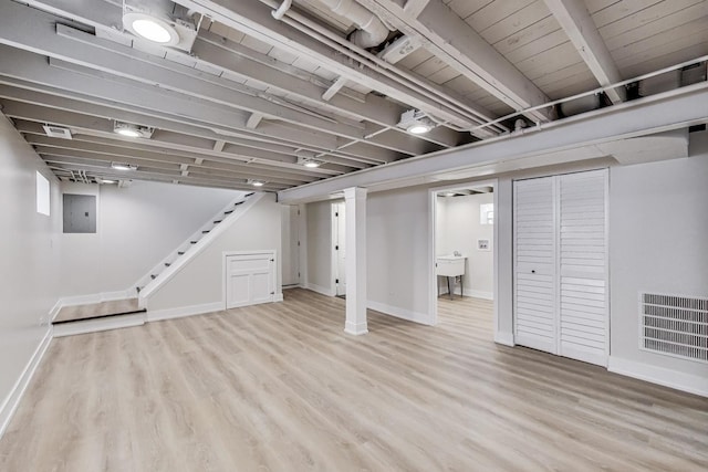 finished basement with light wood-style floors, electric panel, and baseboards