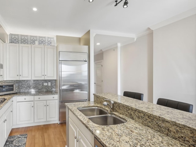 kitchen with a sink, appliances with stainless steel finishes, light wood-type flooring, crown molding, and white cabinetry