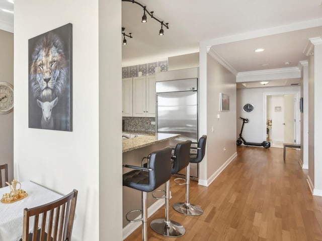 kitchen featuring built in fridge, light wood-style flooring, ornamental molding, a breakfast bar, and baseboards