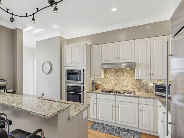 kitchen featuring stainless steel appliances, ornamental molding, a kitchen bar, backsplash, and light stone countertops
