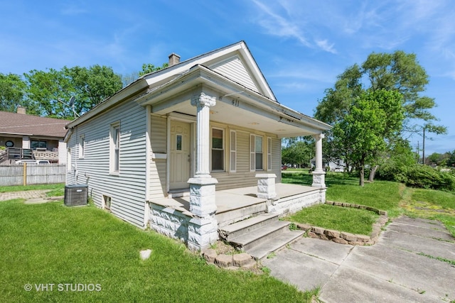 view of front of house featuring a porch, a front lawn, a chimney, and cooling unit