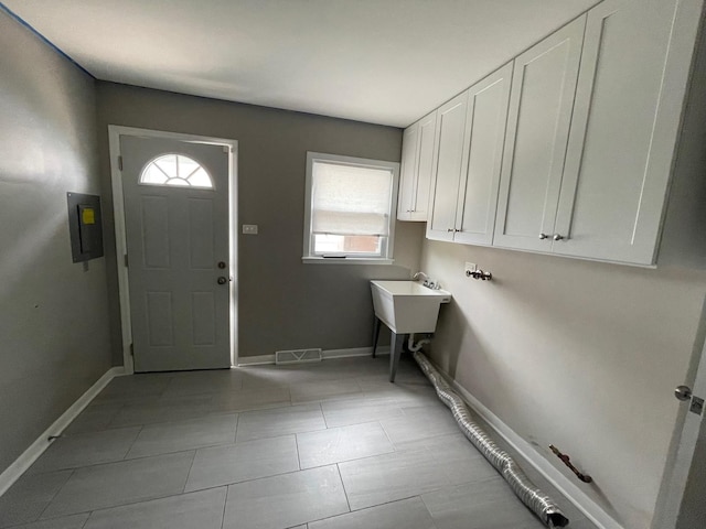 washroom featuring cabinet space, baseboards, electric panel, and light tile patterned floors