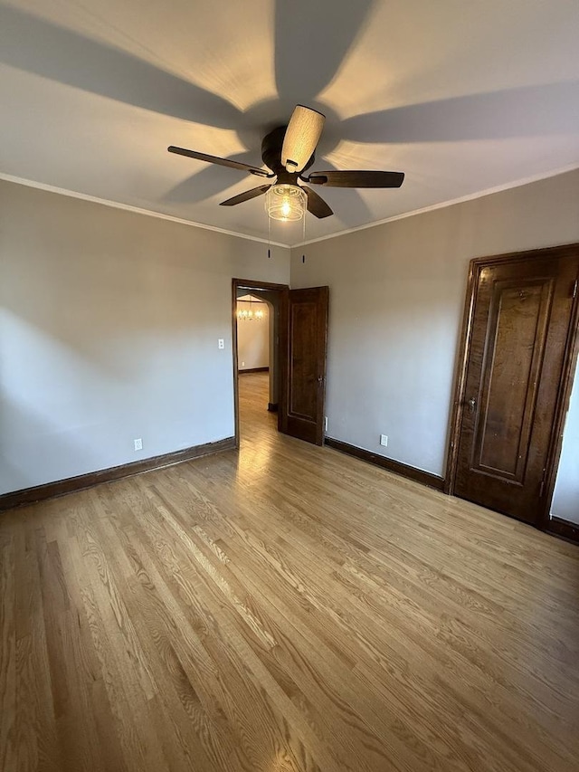 empty room with ceiling fan, baseboards, light wood-type flooring, and crown molding