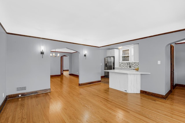 unfurnished living room featuring arched walkways, baseboards, light wood-type flooring, crown molding, and a sink