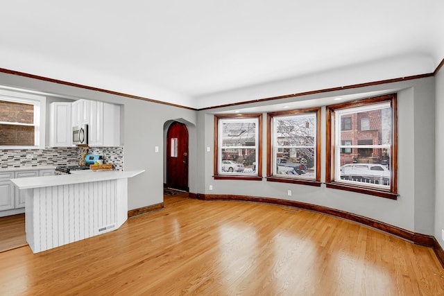 unfurnished living room featuring arched walkways, baseboards, light wood-type flooring, and healthy amount of natural light