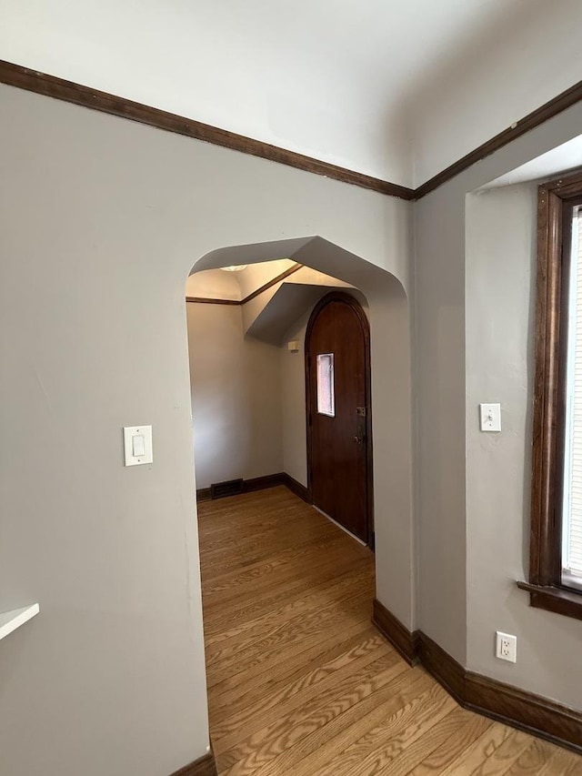 corridor with arched walkways, baseboards, light wood-style flooring, and plenty of natural light
