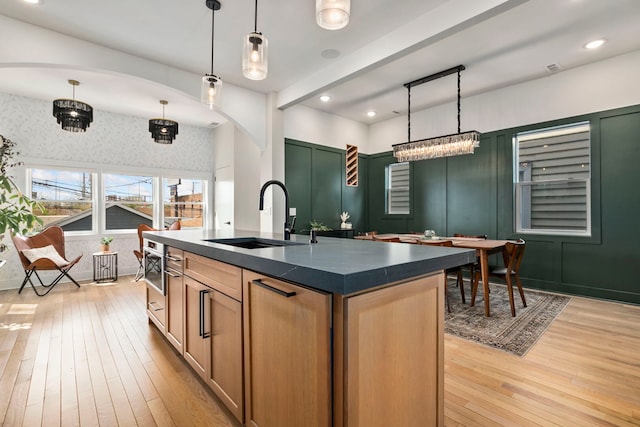 3104 N Sacramento Ave, Chicago, IL 60618 - kitchen with a sink, dark countertops, light wood-style flooring, arched walkways, and hanging light fixtures