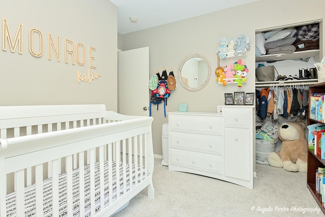bedroom featuring light colored carpet, a nursery area, and a closet