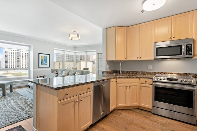 kitchen featuring appliances with stainless steel finishes, light brown cabinets, open floor plan, and a peninsula