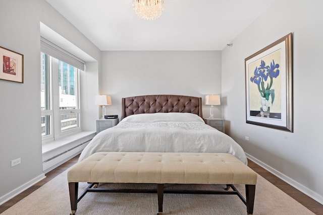 bedroom with a baseboard radiator, dark wood-type flooring, a chandelier, and baseboards