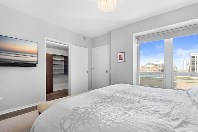 bedroom with baseboards, wood finished floors, a chandelier, a view of city, and a walk in closet