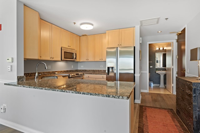 kitchen with stainless steel appliances, a sink, dark wood finished floors, a peninsula, and light brown cabinetry