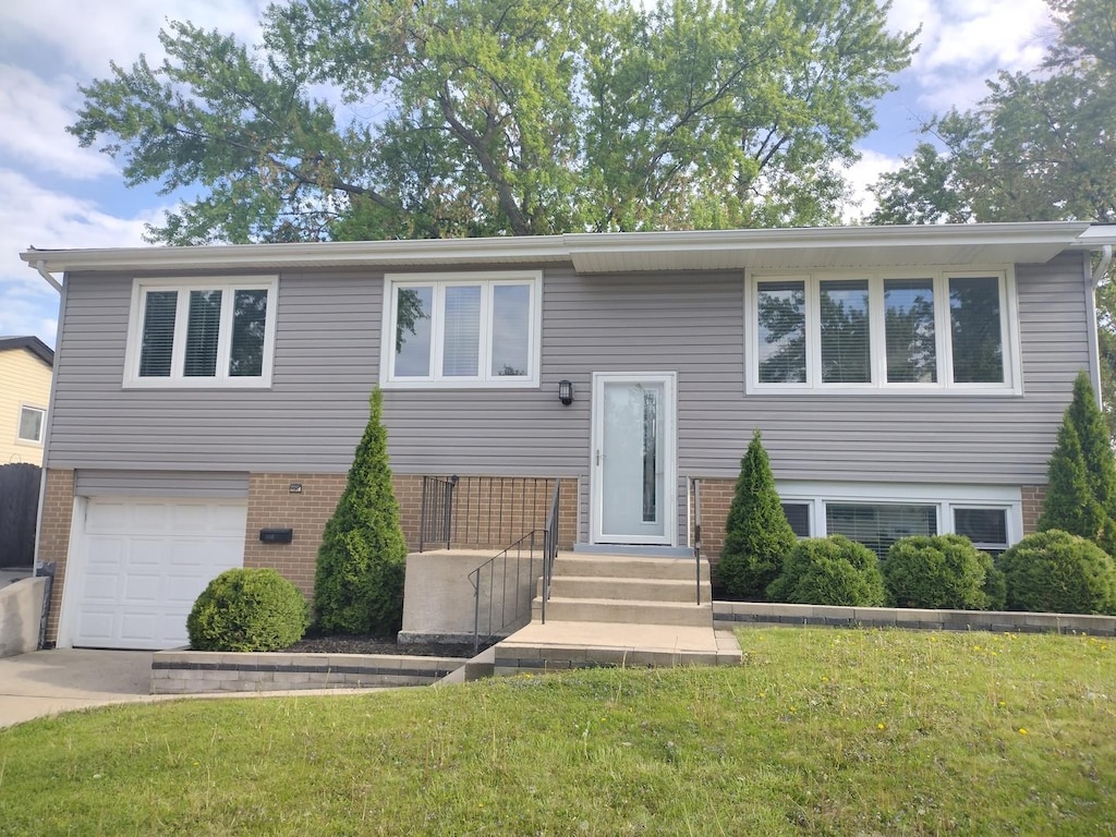 bi-level home with brick siding, a front yard, a garage, and driveway
