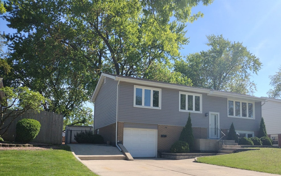 raised ranch featuring brick siding, concrete driveway, an attached garage, and a front lawn