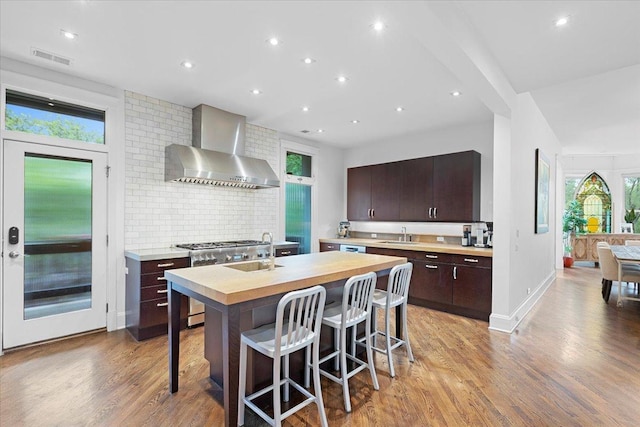 1313 N Wood St Unit 2, Chicago, IL 60622 - kitchen featuring wall chimney range hood, light wood-style flooring, decorative backsplash, a center island with sink, and a sink