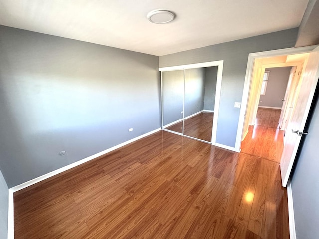 unfurnished bedroom with baseboards, wood finished floors, and a closet
