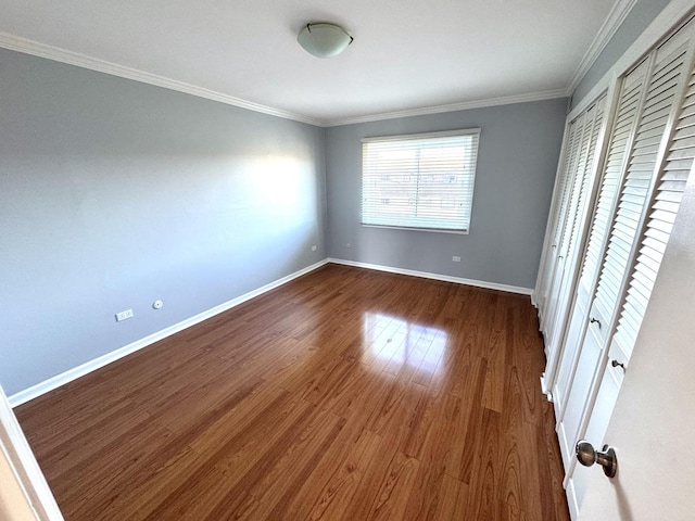 unfurnished bedroom featuring dark wood-style flooring, baseboards, ornamental molding, and two closets