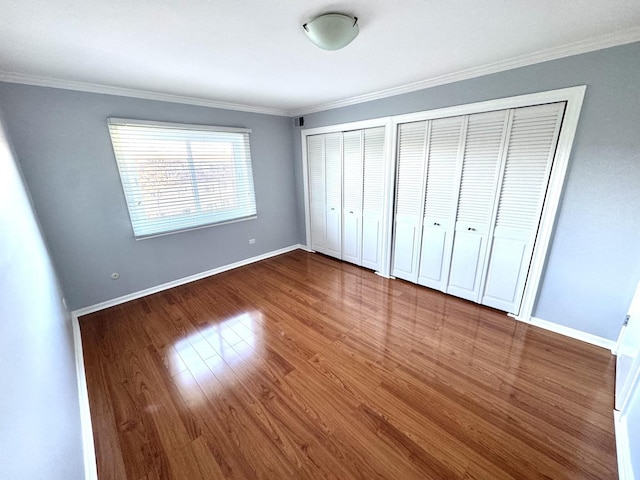 unfurnished bedroom with multiple closets, crown molding, wood finished floors, and baseboards