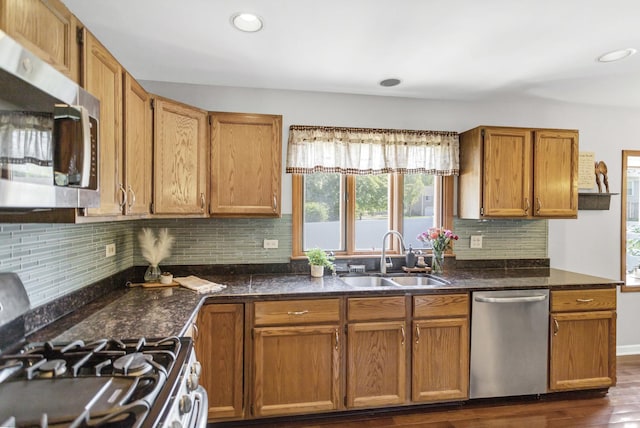 kitchen featuring appliances with stainless steel finishes, a sink, dark wood-style floors, decorative backsplash, and brown cabinets
