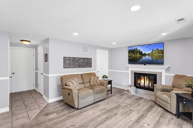 living area with a glass covered fireplace, baseboards, recessed lighting, and light wood finished floors