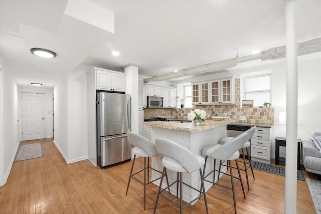 1400 W Thorndale Ave Unit G, Chicago, IL 60660 - kitchen featuring appliances with stainless steel finishes, a breakfast bar, backsplash, light countertops, and glass insert cabinets