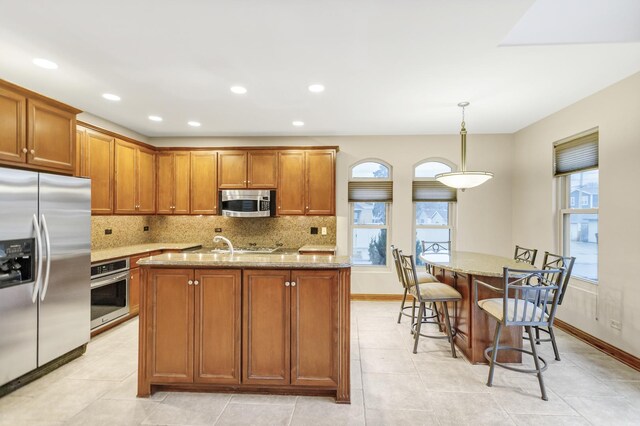5301 S Mobile Ave, Chicago, IL 60638 - kitchen with stainless steel appliances, a kitchen island with sink, brown cabinets, light stone counters, and backsplash