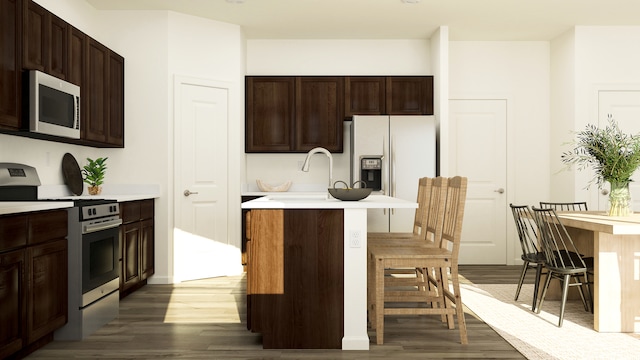 kitchen with stainless steel appliances, dark wood-style floors, a kitchen bar, light countertops, and a center island with sink