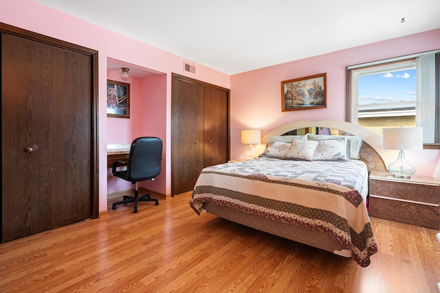bedroom with two closets, light wood finished floors, an office area, and baseboards
