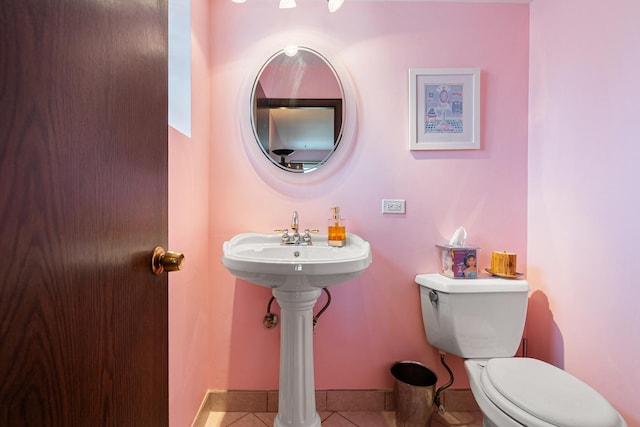 half bath with baseboards, toilet, and tile patterned flooring
