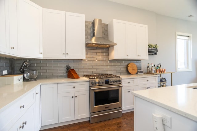 kitchen featuring wall chimney range hood, high end range, backsplash, and white cabinets