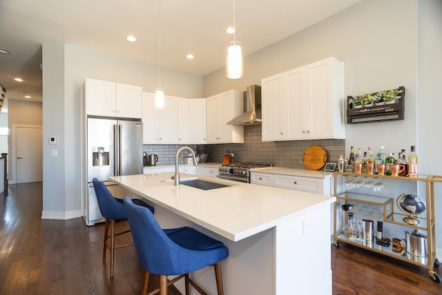 kitchen featuring high quality appliances, wall chimney range hood, a sink, decorative backsplash, and dark wood-style floors