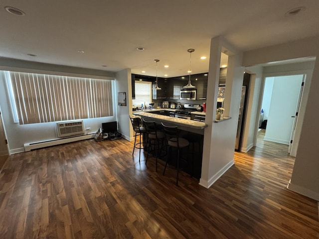 kitchen with appliances with stainless steel finishes, baseboard heating, dark wood-type flooring, light countertops, and a breakfast bar
