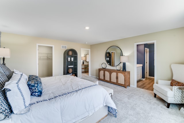 carpeted bedroom featuring a walk in closet, baseboards, a closet, and ensuite bath