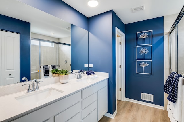 full bathroom with a shower stall, wood finished floors, double vanity, and baseboards