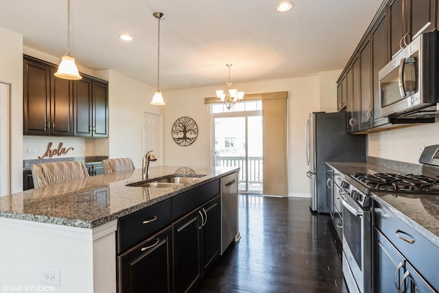 kitchen with stainless steel appliances, a sink, dark stone countertops, dark wood-style floors, and an island with sink