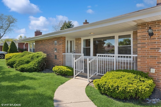 6502 Palma Ln, Morton Grove, IL 60053 - doorway to property with a chimney, brick siding, covered porch, and a lawn