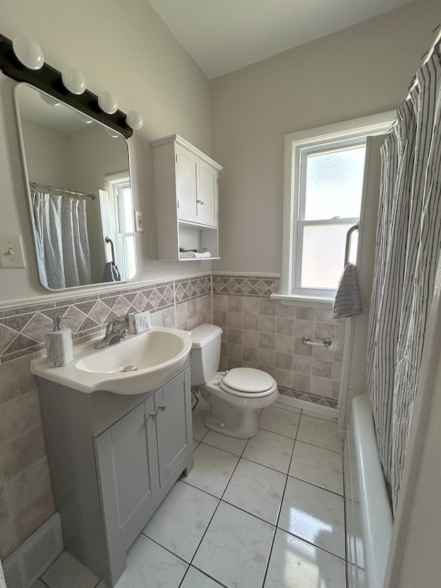 650 Enterprise St, Elgin, IL 60120 - bathroom with tile walls, vanity, a wainscoted wall, toilet, and shower / tub combo with curtain