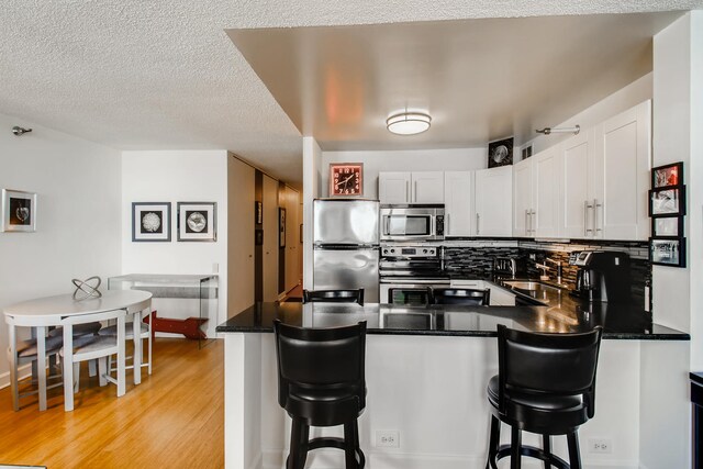 474 N Lake Shore Dr Unit 2012, Chicago, IL 60611 - kitchen with appliances with stainless steel finishes, a sink, a peninsula, dark countertops, and light wood-style flooring