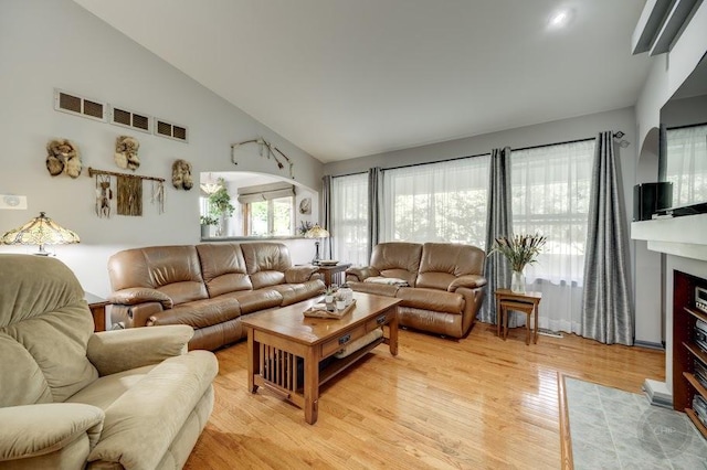 living room featuring light wood finished floors, high vaulted ceiling, and a fireplace with flush hearth