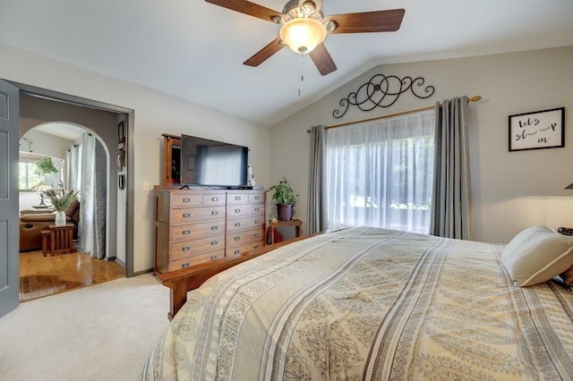 carpeted bedroom featuring vaulted ceiling, arched walkways, and a ceiling fan