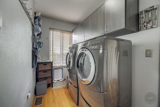 washroom with cabinet space, washer and clothes dryer, and light wood-style floors