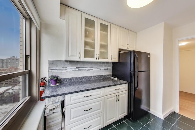 kitchen featuring freestanding refrigerator, dark tile patterned flooring, tasteful backsplash, glass insert cabinets, and white cabinets