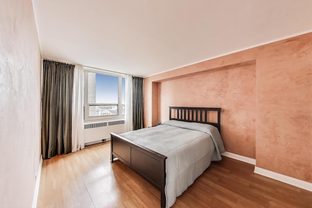 bedroom featuring radiator heating unit, wood finished floors, and baseboards