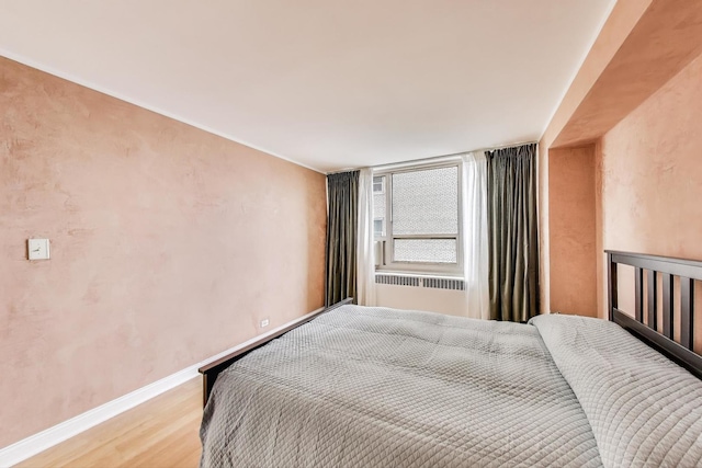 bedroom featuring light wood-type flooring, baseboards, and radiator