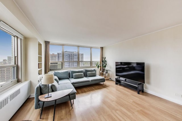 living area with radiator heating unit, a view of city, light wood-type flooring, baseboards, and cooling unit