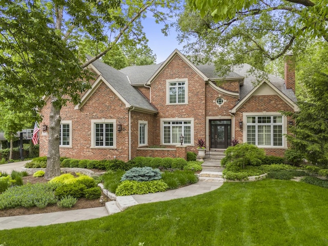 view of front of property featuring a front lawn, brick siding, a chimney, and a shingled roof