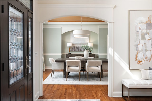 dining space with arched walkways, ornamental molding, wood finished floors, and baseboards